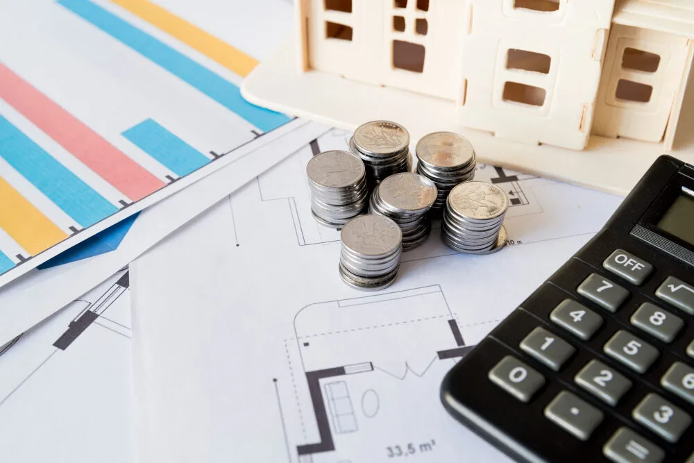 Texas MUD financing solutions shown with coins, calculator, and house model on architectural plans, illustrating MUD distr...
