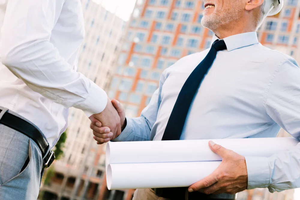 Two businessmen shaking hands with blueprints, discussing Texas MUD financing options and MUD district funding solutions.