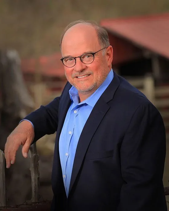 Man in a suit leaning on a fence with a blurred background, representing expertise in Texas MUD financing and MUD district...